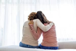 Rear view of mother and daughter embracing sitting on bed