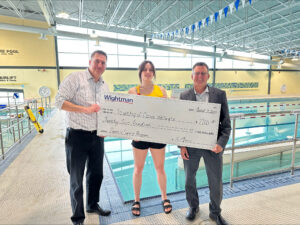 Three individuals holding a large cheque standing beside the Fergus Public Pool.